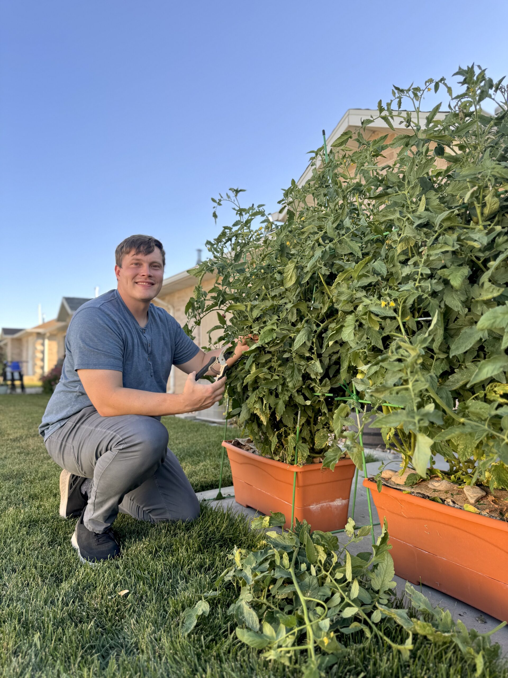 Real Farmer Jeff bending to harvest ripe vegetables from large containers, highlighting productive container gardening in limited space.