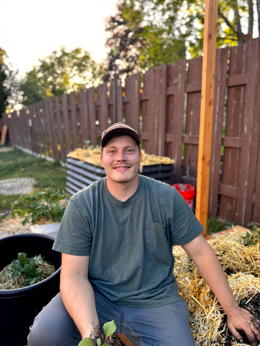 Jeff smiling in a thriving home garden surrounded by green leafy plants, representing Farmerxfoodie's passion for sustainable gardening.