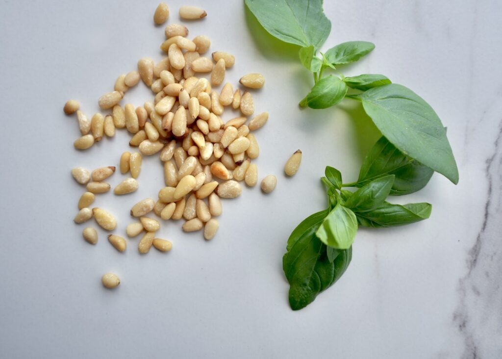 Pine nuts and fresh basil on marble counter for homemade lemon basil pesto recipe.