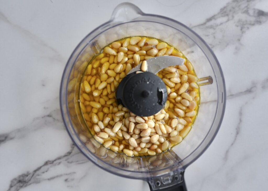 Pine nuts soaking in olive oil in food processor for homemade pesto sauce.