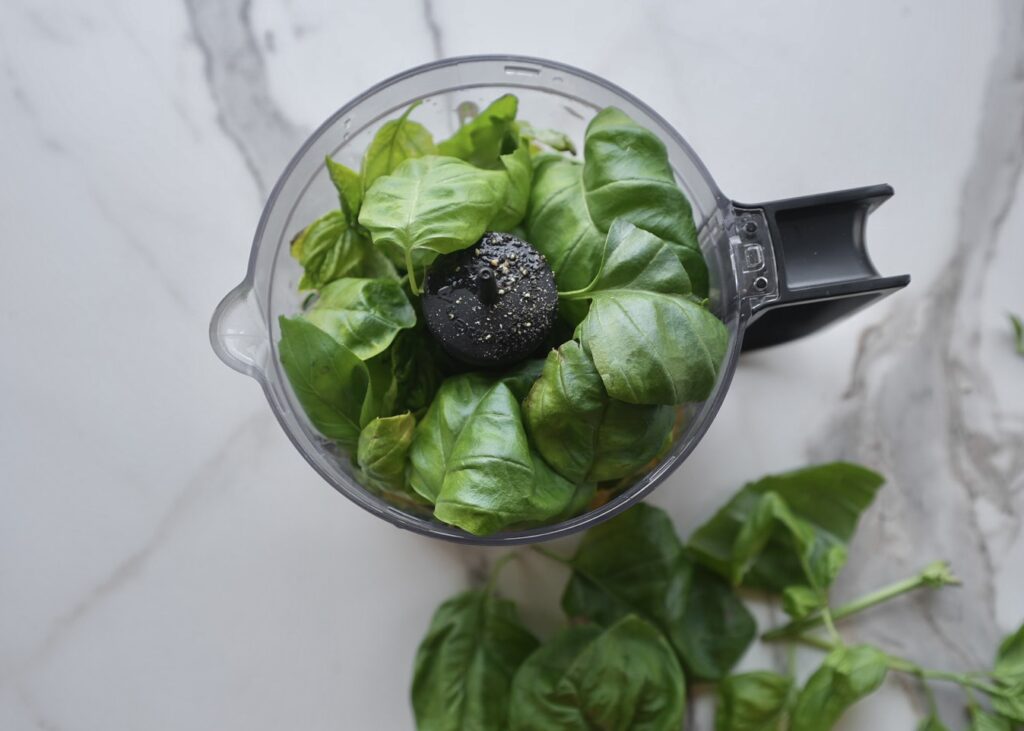 Fresh basil in food processor as key ingredient for lemon pesto pasta sauce.