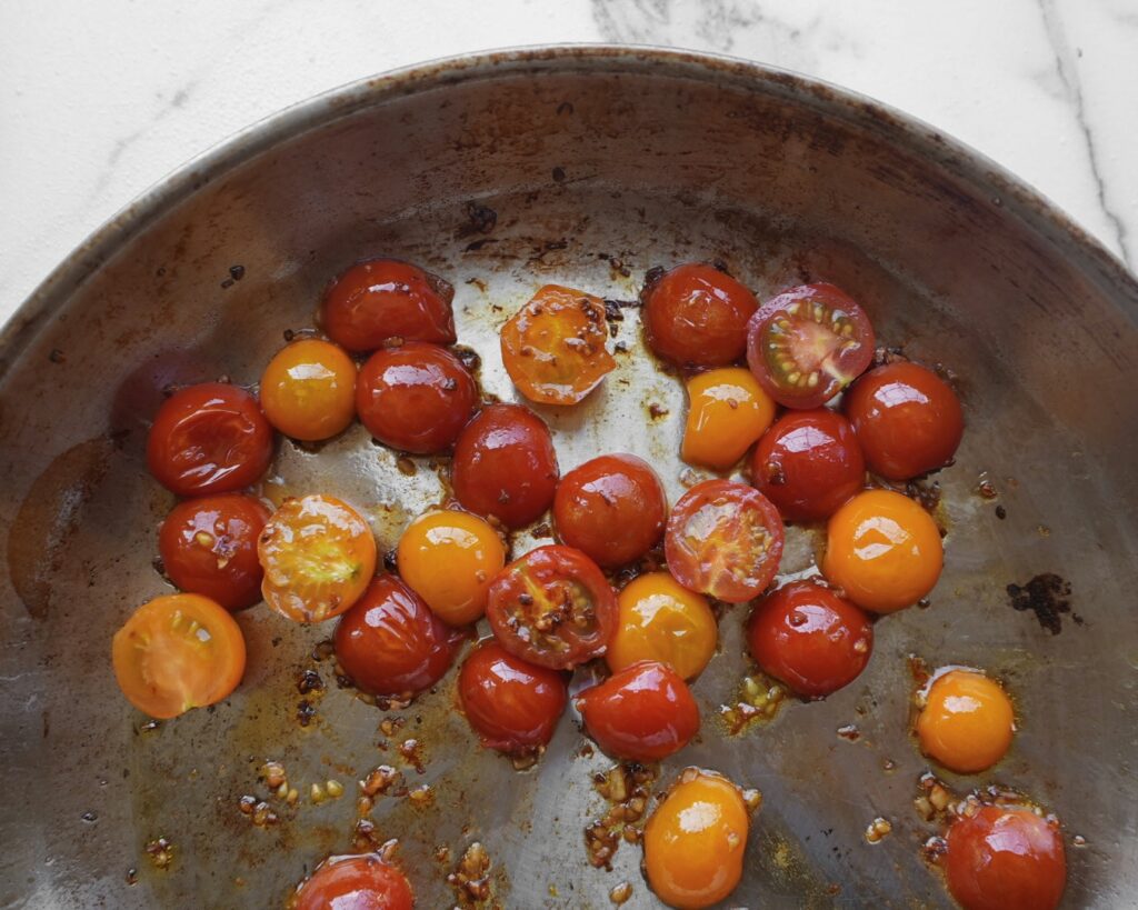 Skillet of roasted cherry tomatoes and garlic for lemon pesto pasta recipe.